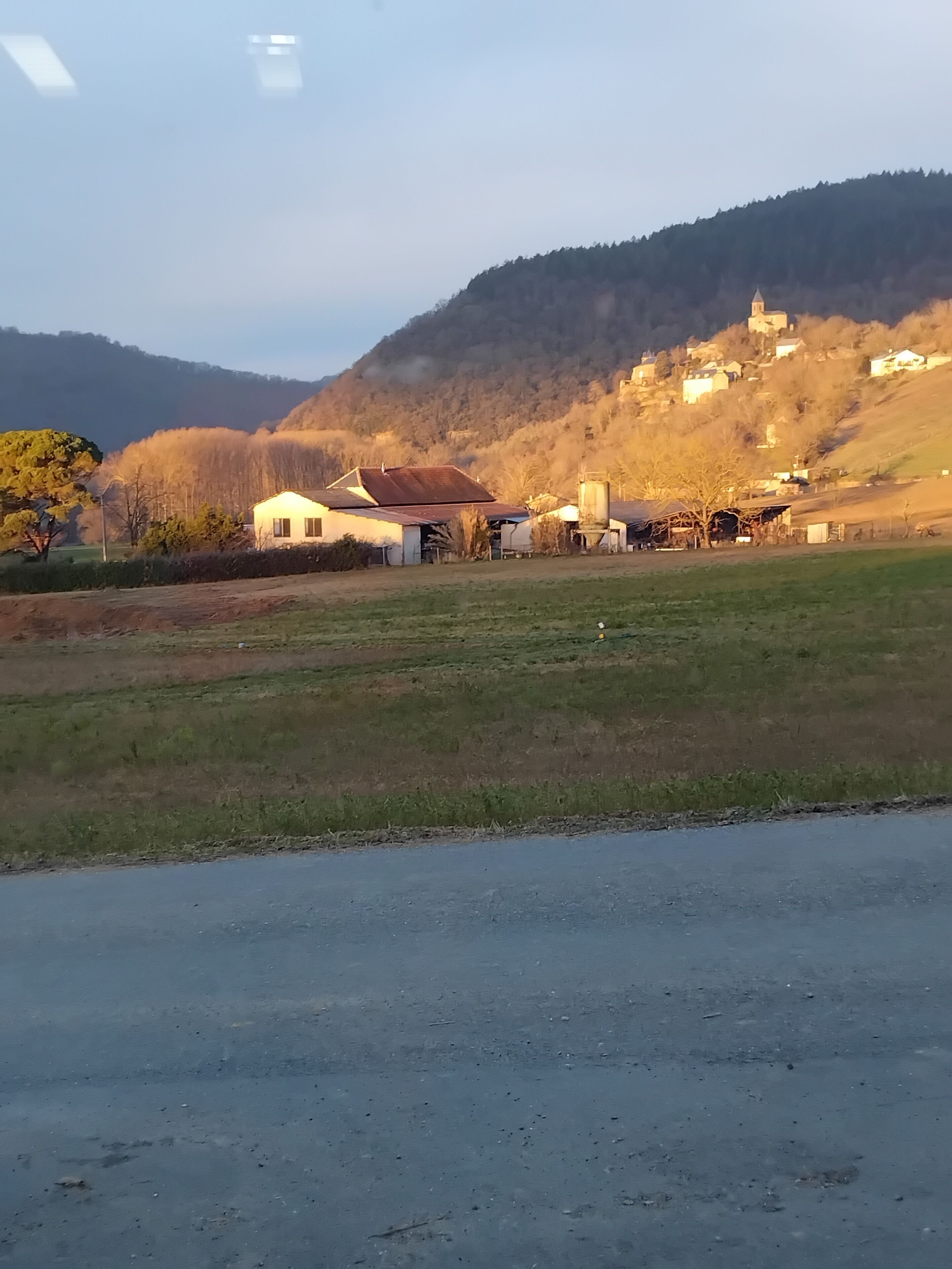 Un paysage rural avec une route, des bâtiments et une colline sur laquelle se trouve une église.