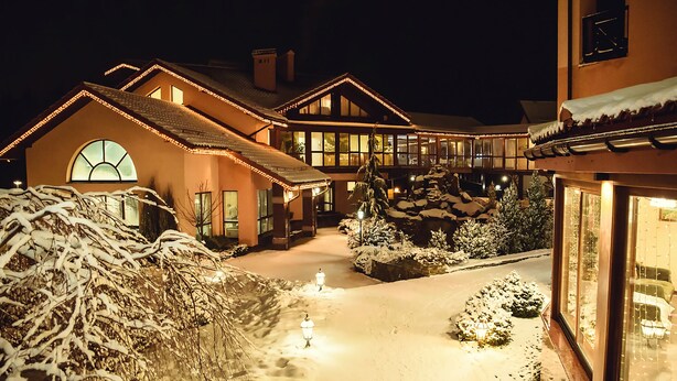 Un patio nevado con un sendero que conduce a un edificio con ventanas amplias y un elemento decorativo de piedra.