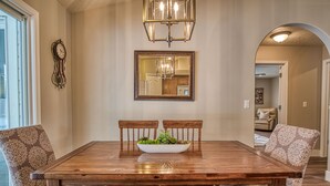 A dining area with a wooden table, two chairs, a chandelier, a clock, and a mirror on the wall. - Cozy and Stylish Home (Boise)