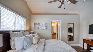 A bedroom with a large bed, a ceiling fan, a painting, a mirror, and a TV. - Cozy and Stylish Home (Boise)