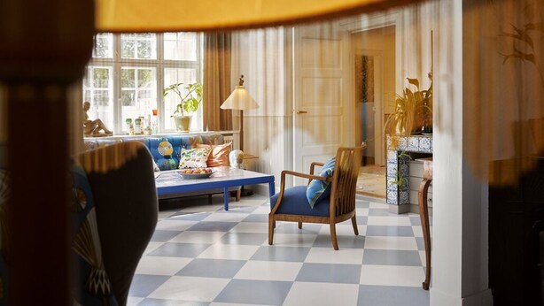 A checkered floor, a blue sofa, a wooden chair, a lamp, and a window with curtains. - Hotel Villa Strand (Hornbaek)