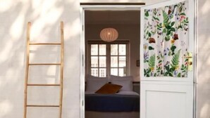 A room with a wooden ladder leaning against a wall, a bed with a blue bedspread, and a window with a view of the outside. - Hotel Villa Strand (Hornbaek)