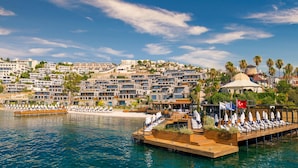 A waterfront hotel with multiple balconies overlooking the sea, a wooden deck with lounge chairs, and a flag indicating Turkish location. - The Norm Le Chic (Bodrum)