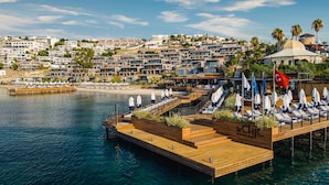 A waterfront hotel with a wooden deck, lounge chairs, and umbrellas. - The Norm Le Chic (Bodrum)