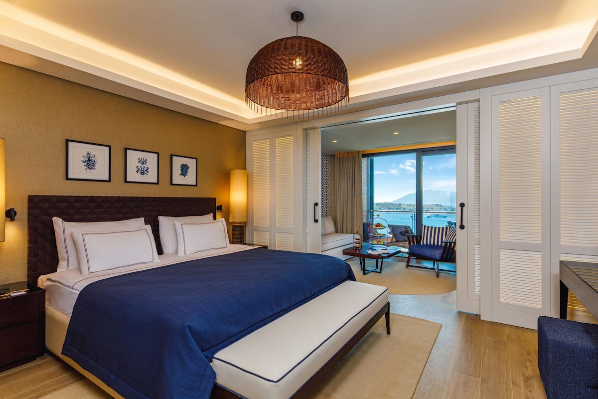 Une chambre d’hôtel moderne dotée d’un grand lit, offrant une vue sur la mer et comprenant un balcon avec des sièges d’extérieur.