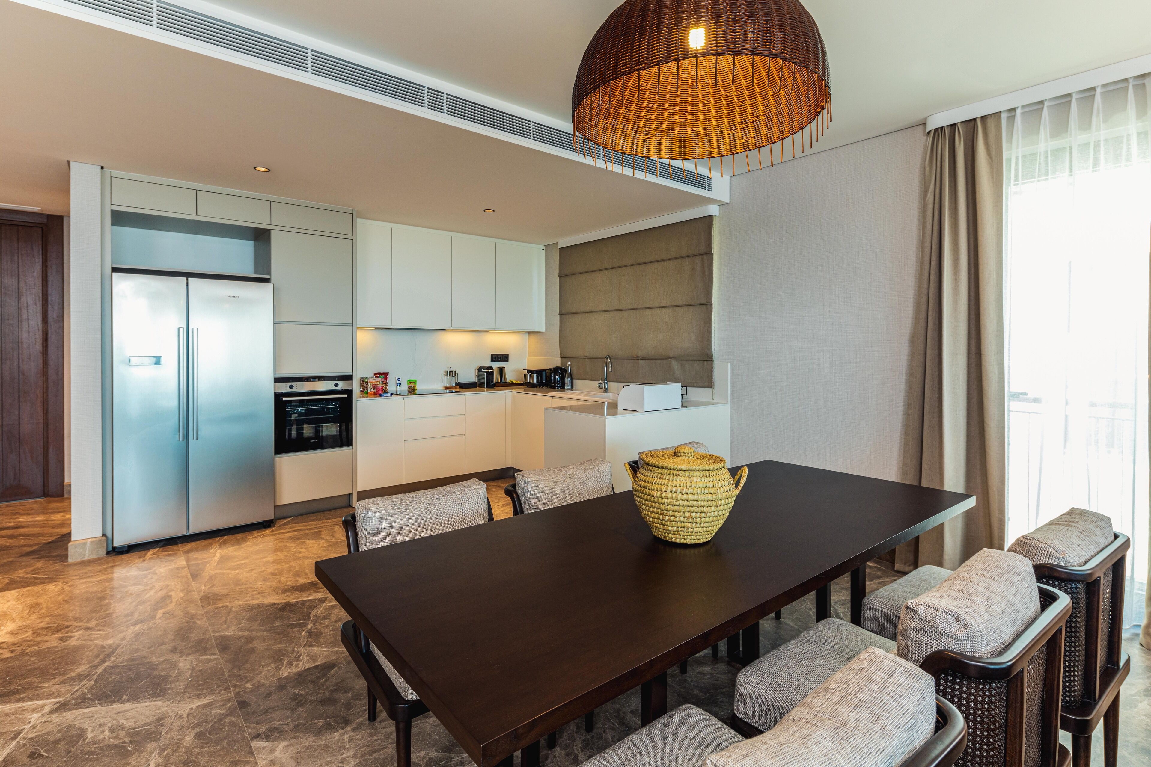 A modern kitchen with a dining area, featuring a large table, chairs, and a woven basket centerpiece.