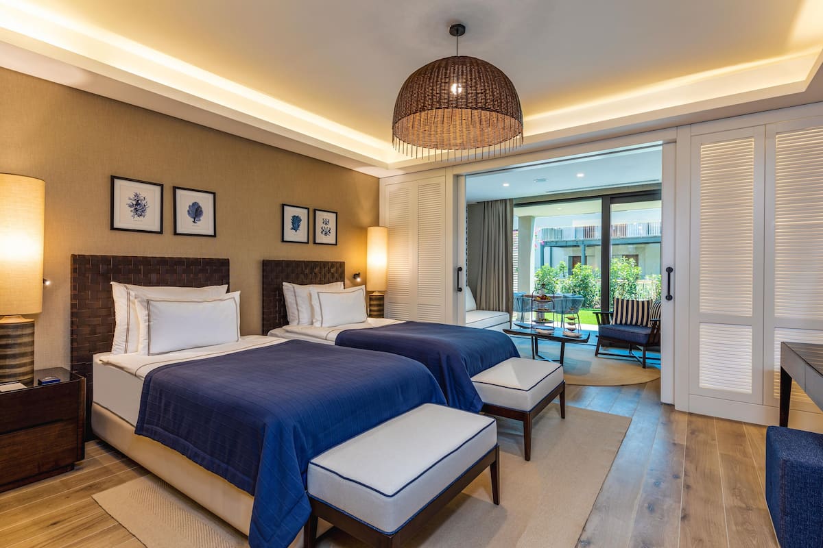 Une chambre d’hôtel avec deux lits, une grande fenêtre, un coin repas et une vue sur l’extérieur.