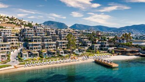 A coastal resort with modern buildings, a beach, and a pier. - The Norm Le Chic (Bodrum)