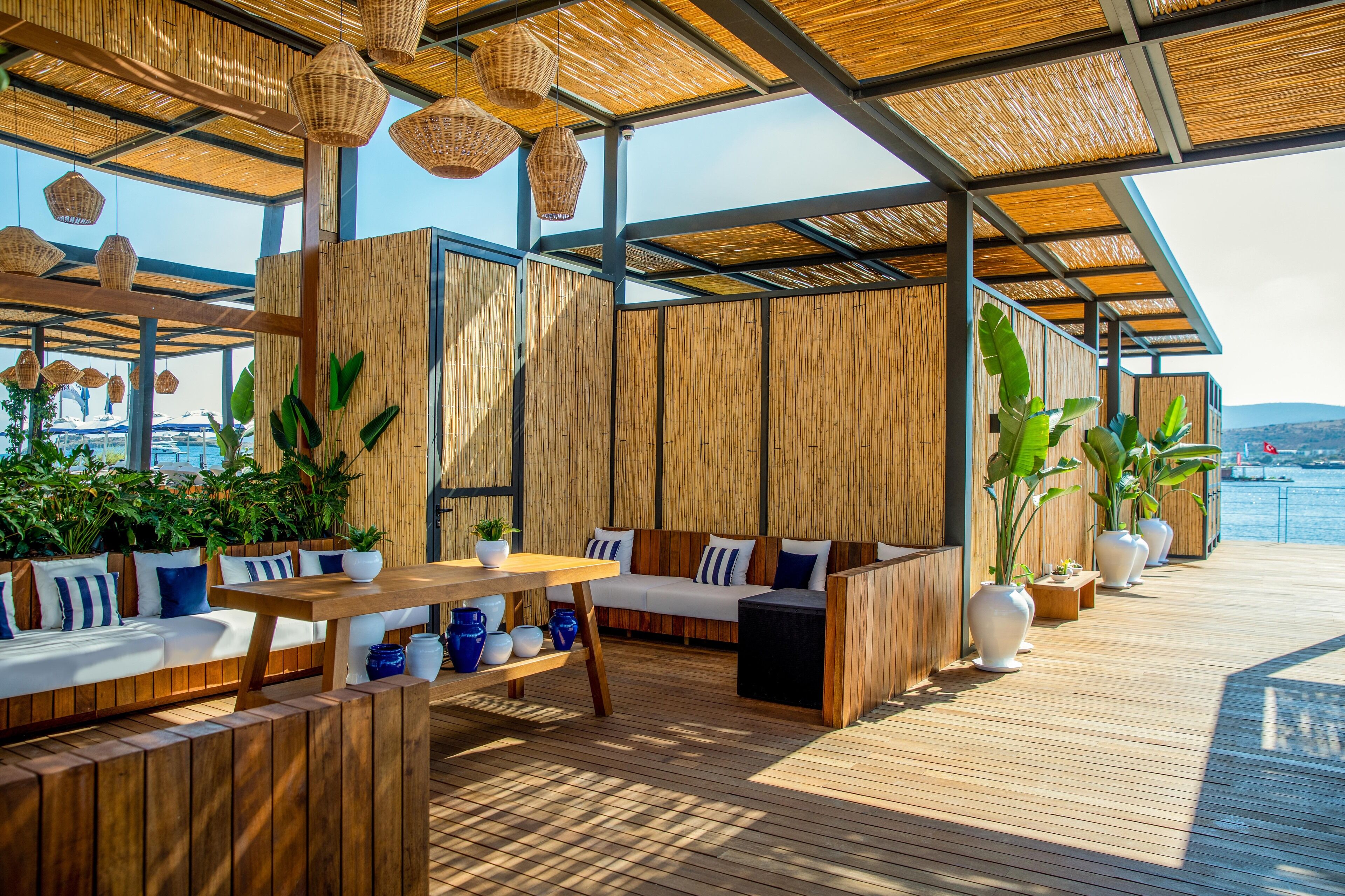 Een houten terras met een bank, tafels en potplanten.