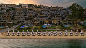 A coastal hotel with multiple buildings, a beach with sun loungers, and swimming pools. - The Norm Le Chic (Bodrum)