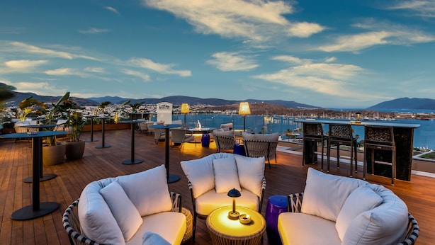 A rooftop terrace with outdoor seating, a view of the sea, and distant mountains. - The Norm Le Chic (Bodrum)