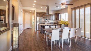 A modern kitchen with dark wood cabinets, stainless steel appliances, and a dining area with white chairs and a wooden table. - Modern 3BR on the 18th Green - Golf Course Views (St. George)