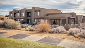 A modern multi-story building with a flat roof and large windows, surrounded by dry shrubs and a paved walkway. - Modern 3BR on the 18th Green - Golf Course Views (St. George)