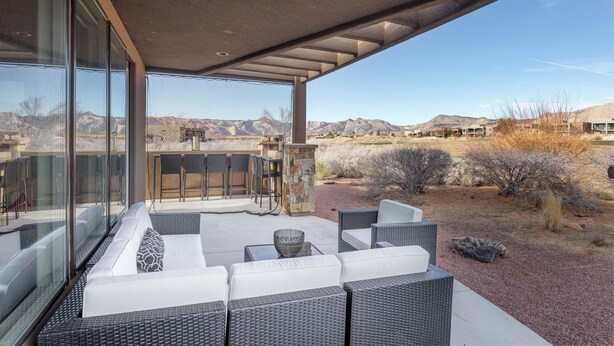 A modern outdoor patio with seating and a bar area, overlooking a desert landscape. - Modern 3BR on the 18th Green - Golf Course Views (St. George)