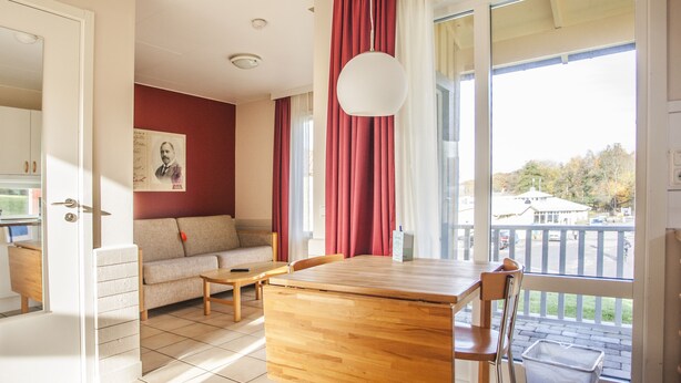 A room with a wooden table, a sofa, and a view of a balcony.