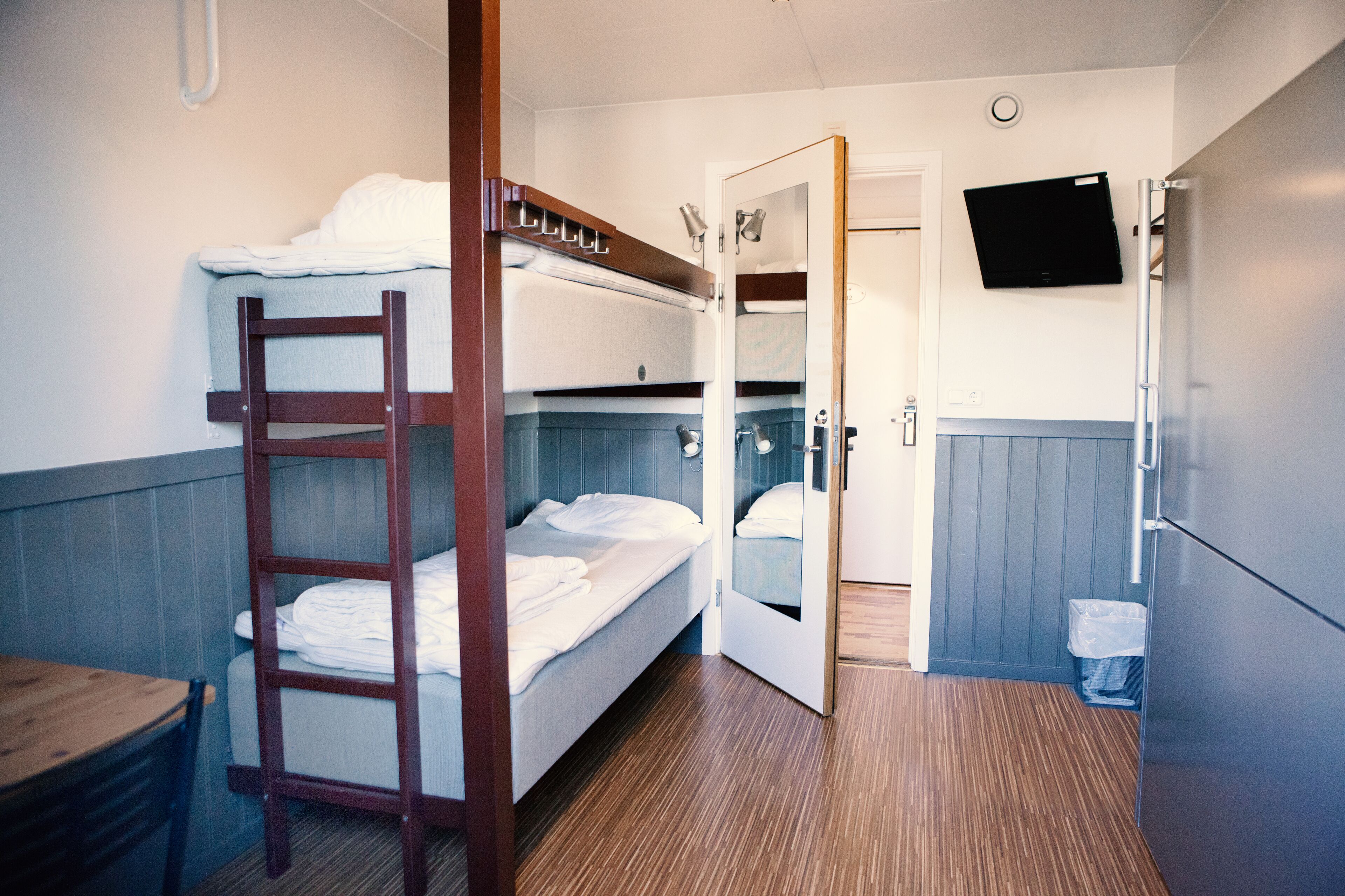 Une chambre avec un lit superposé, une échelle en bois, une petite table et une poubelle.