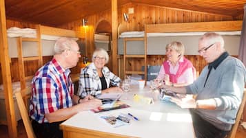 Interior de una cabaña de madera con literas, una mesa de comedor con revistas y una botella de vino.