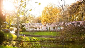A row of cabins with a pond in the foreground, surrounded by trees and a fence.