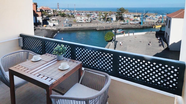 A balcony with wicker chairs and a table, overlooking a marina with boats and a beach. - Central with sea views from the terrace. Pool and free wifi. (Puerto de la Cruz)
