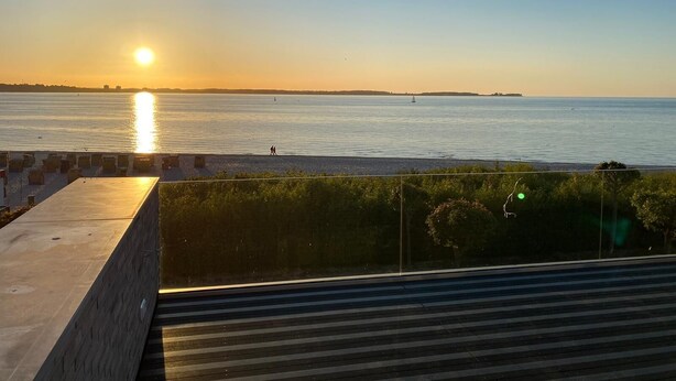 A sunset view from a balcony overlooking a beach with a calm sea, a distant ship, and a clear sky. - Apartment Sontje the first time OG (Laboe)