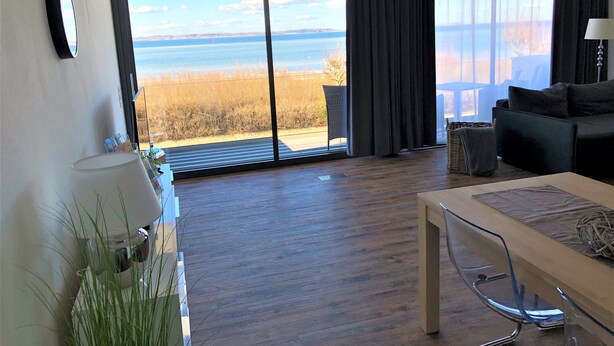 A modern living room with a large sliding glass door leading to a balcony with a view of the sea. - Apartment Eltje on the 1st floor (Laboe)