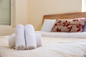 A neatly made bed with rolled white towels and a floral pillow. - Modern & Stylish 3BR Apt With Balcony (Tel Aviv)