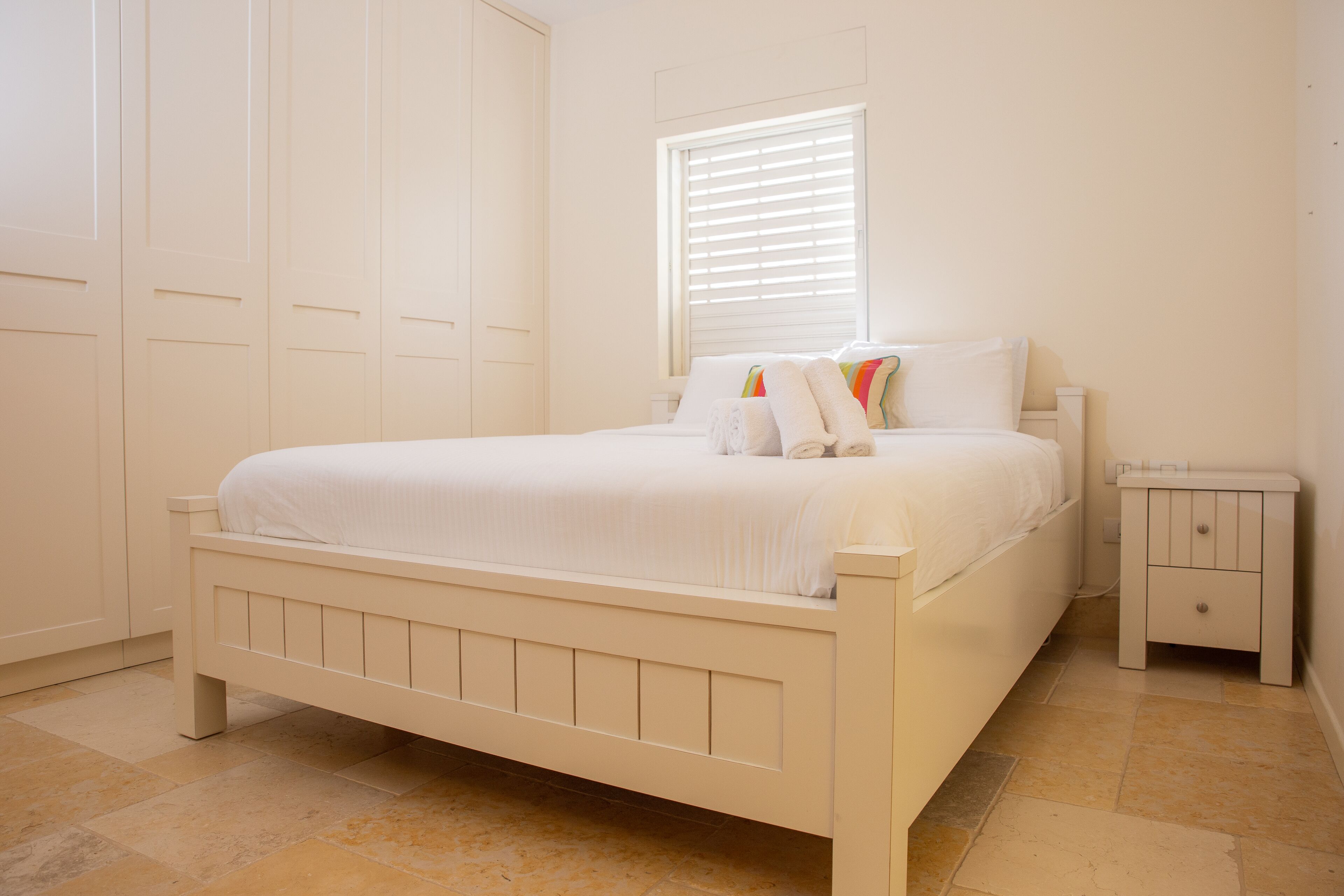 A bedroom with a white bed, a nightstand, and a wardrobe.