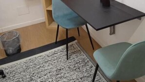 Een kleine, moderne kamer met een donkerhouten tafel, twee stoelen, een blauwe stoel, een houten plank en een prullenbak.