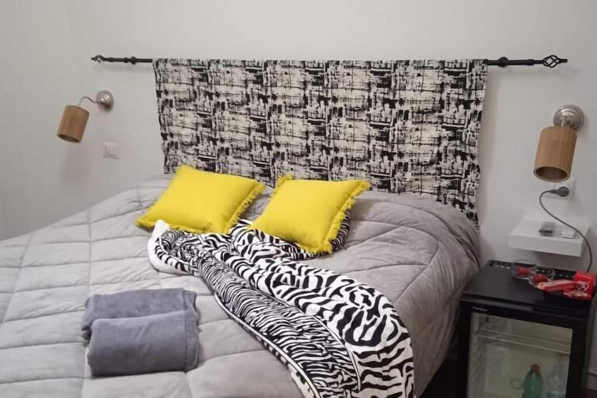 A bed with a zebra-patterned blanket, two yellow pillows, and a grey quilted duvet.