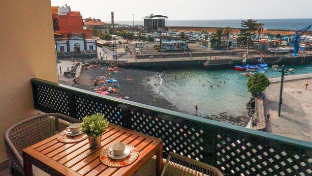 Ein Balkon mit Holztisch und Stühlen, der auf einen belebten Hafen mit Booten und einem Strand blickt.