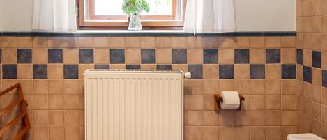 A bathroom with a toilet, a radiator, a window with curtains, and a towel rack.