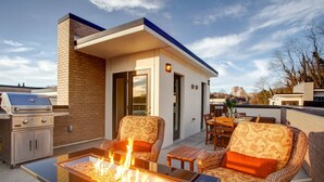 Eine Dachterrasse mit Grill, Gartenmöbeln und einer Feuerstelle.
