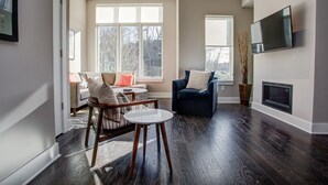 Ein modernes Wohnzimmer mit dunklem Holzboden, einem runden Tisch, einem blauen Sessel und einer Couch mit Kissen.