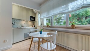 A modern kitchen with white cabinetry, a dining table with chairs, and a view of greenery outside. - Studio 4* center near Kirchberg, quiet with view (Luxembourg)