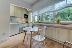 A modern kitchen with white cabinetry, a dining table with chairs, and a view of greenery outside.