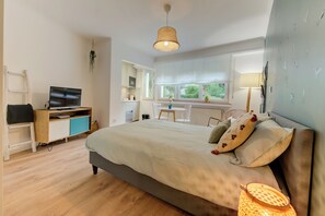 A bedroom with a bed, a desk, a television, and a window with a view of greenery. - Studio 4* center near Kirchberg, quiet with view (Luxembourg)