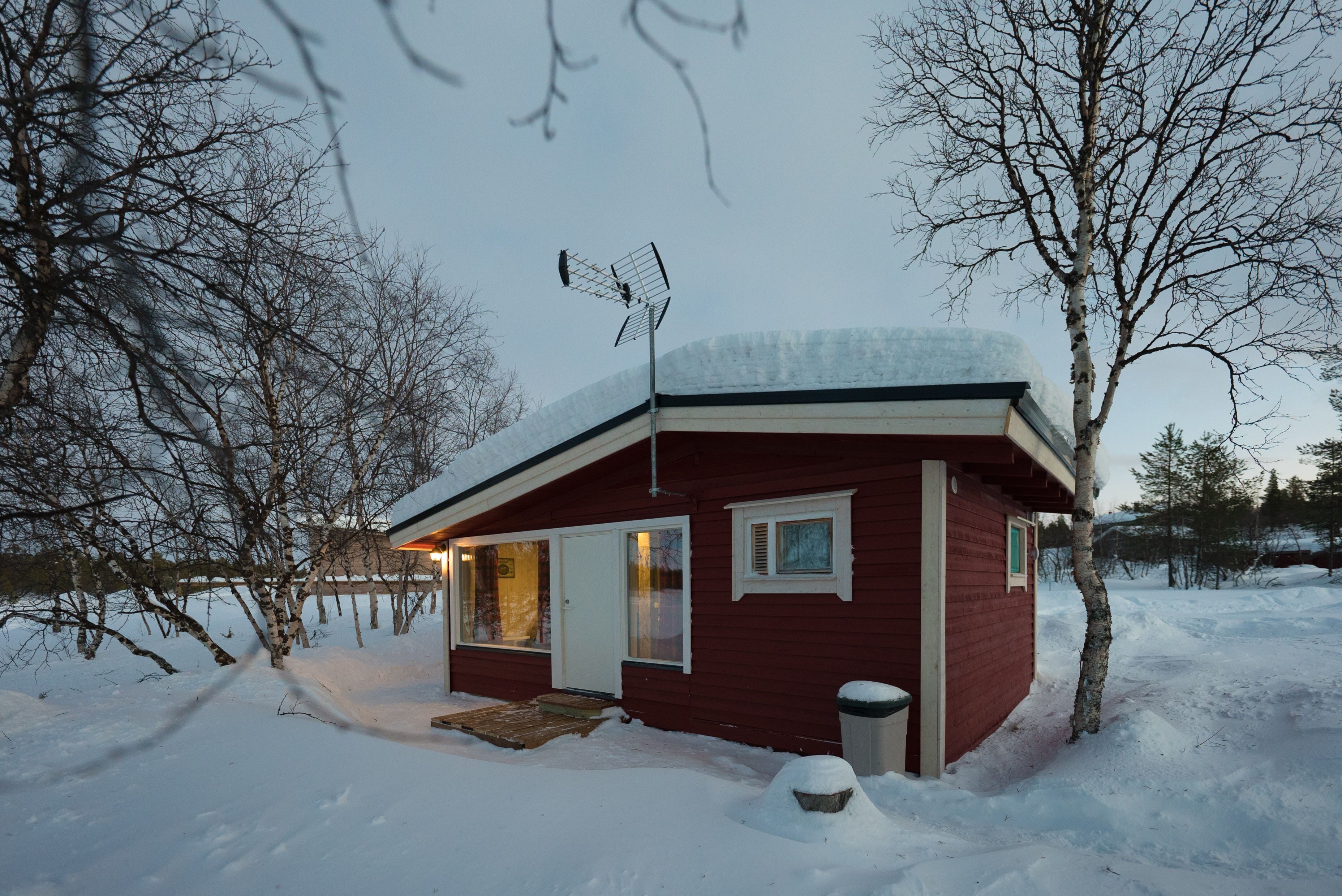 A small, red cabin with a snow-covered roof, a wooden door, and a window.