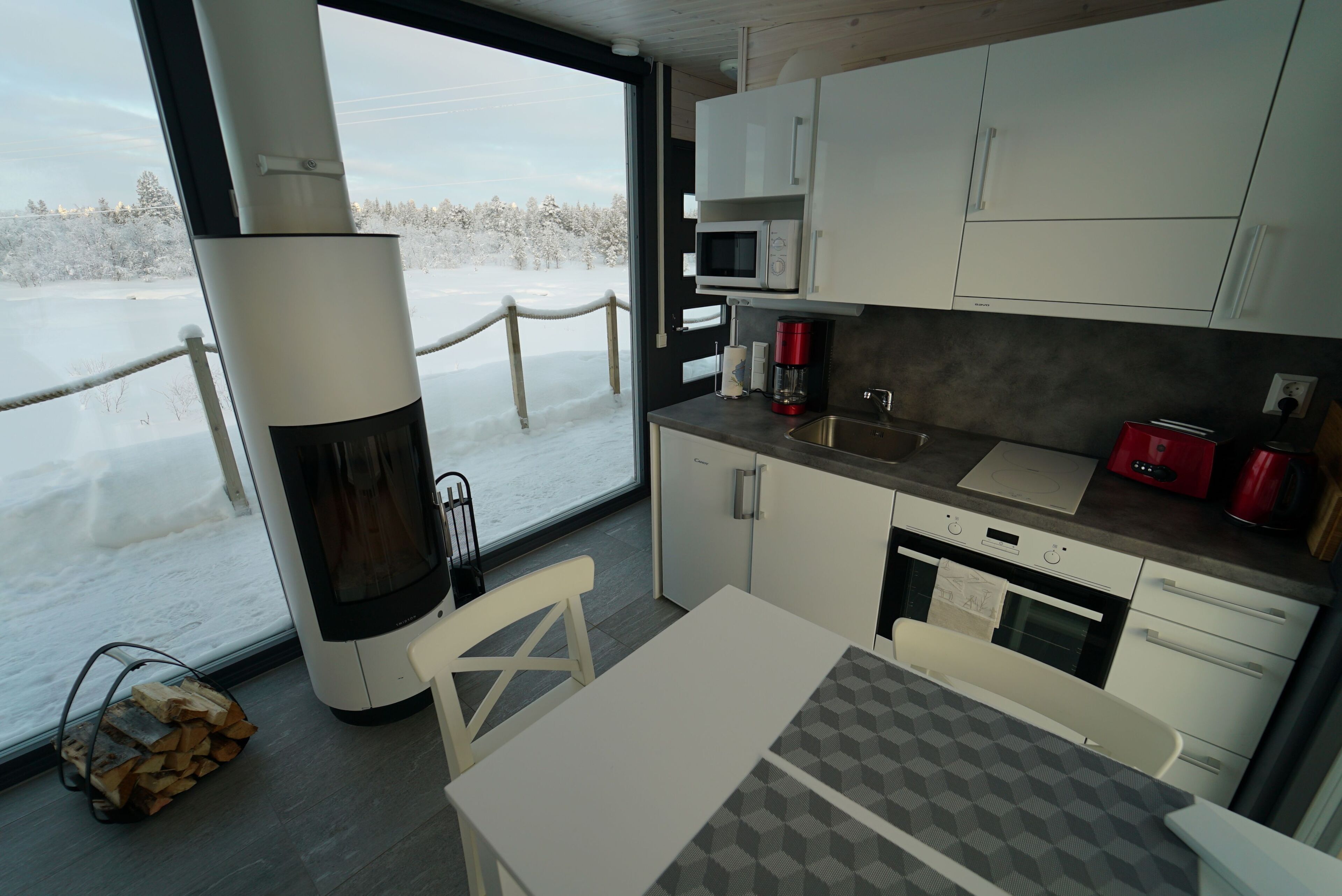 A modern kitchen with white cabinets, a microwave, a coffee maker, and a view of a snowy landscape.