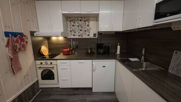 Cocina compacta con armarios blancos, horno empotrado, lavavajillas y microondas.
