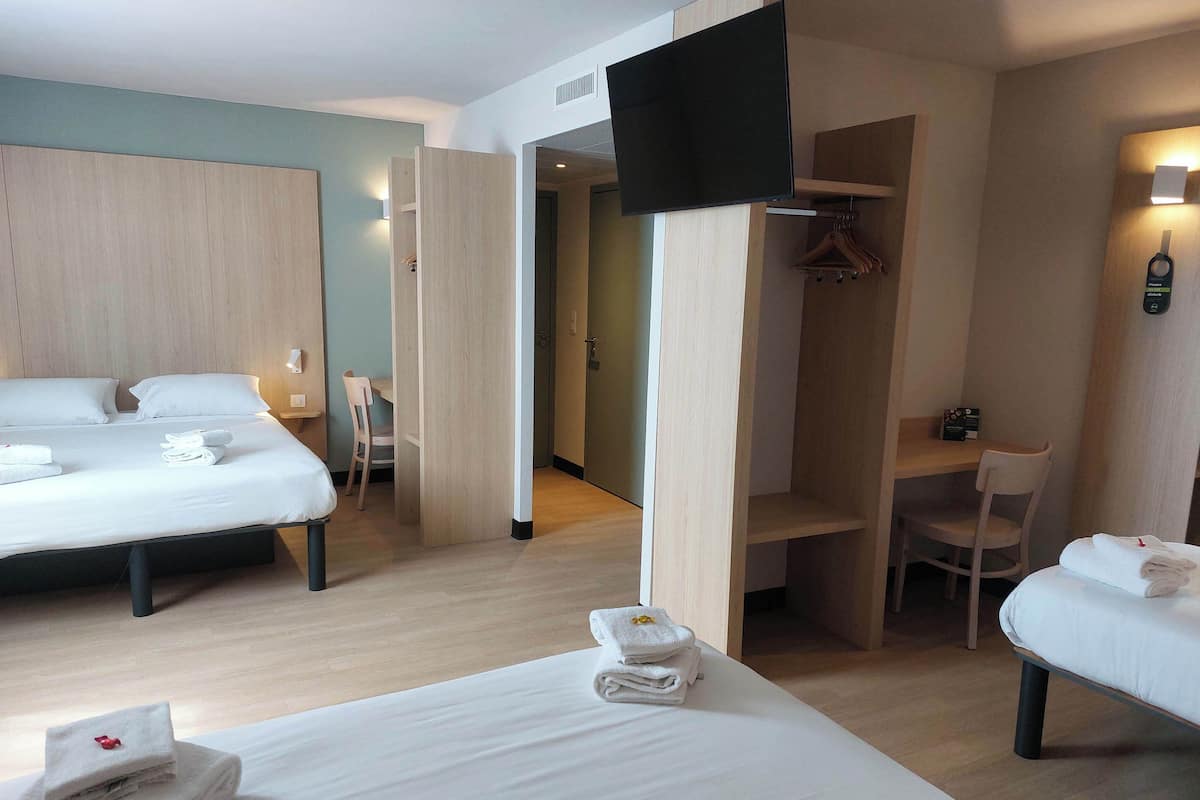 A hotel room with two beds, a TV, a wardrobe, and a desk.