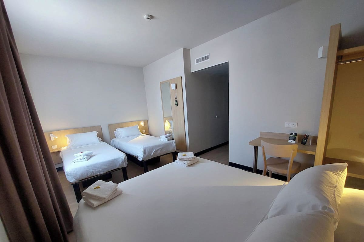 A hotel room with two beds, a desk, a chair, and a mirror.