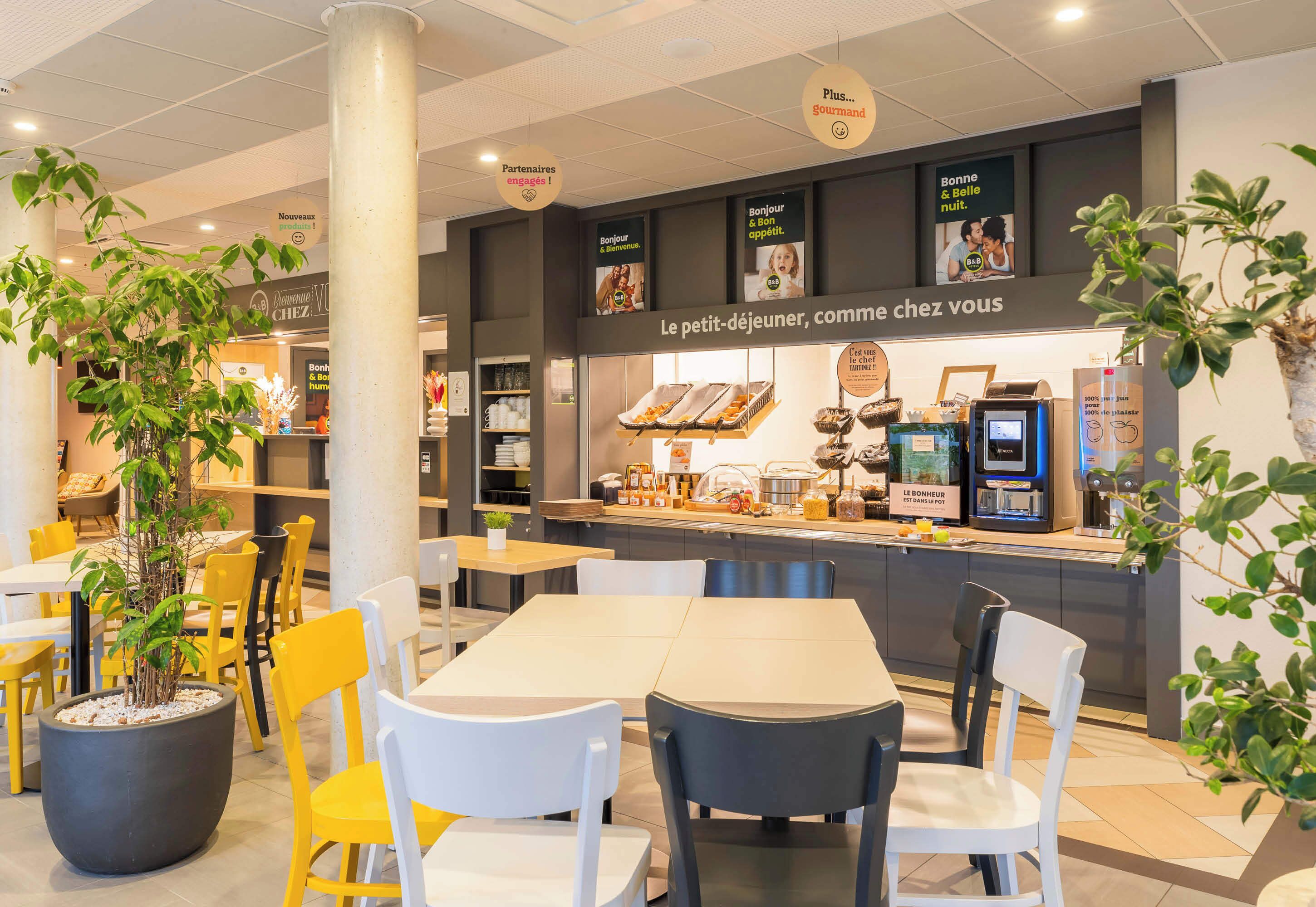 A café with a counter displaying pastries and coffee machines, surrounded by yellow and white chairs.