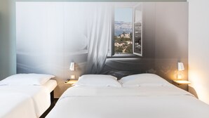Hotellihuone, jossa on kaksi sänkyä, suuri ikkuna, josta avautuu näkymä vuoristomaisemaan, sekä yöpöytävalaisimet.