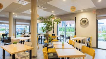A modern indoor dining area with tables and chairs, large windows, and a decorative wall clock.