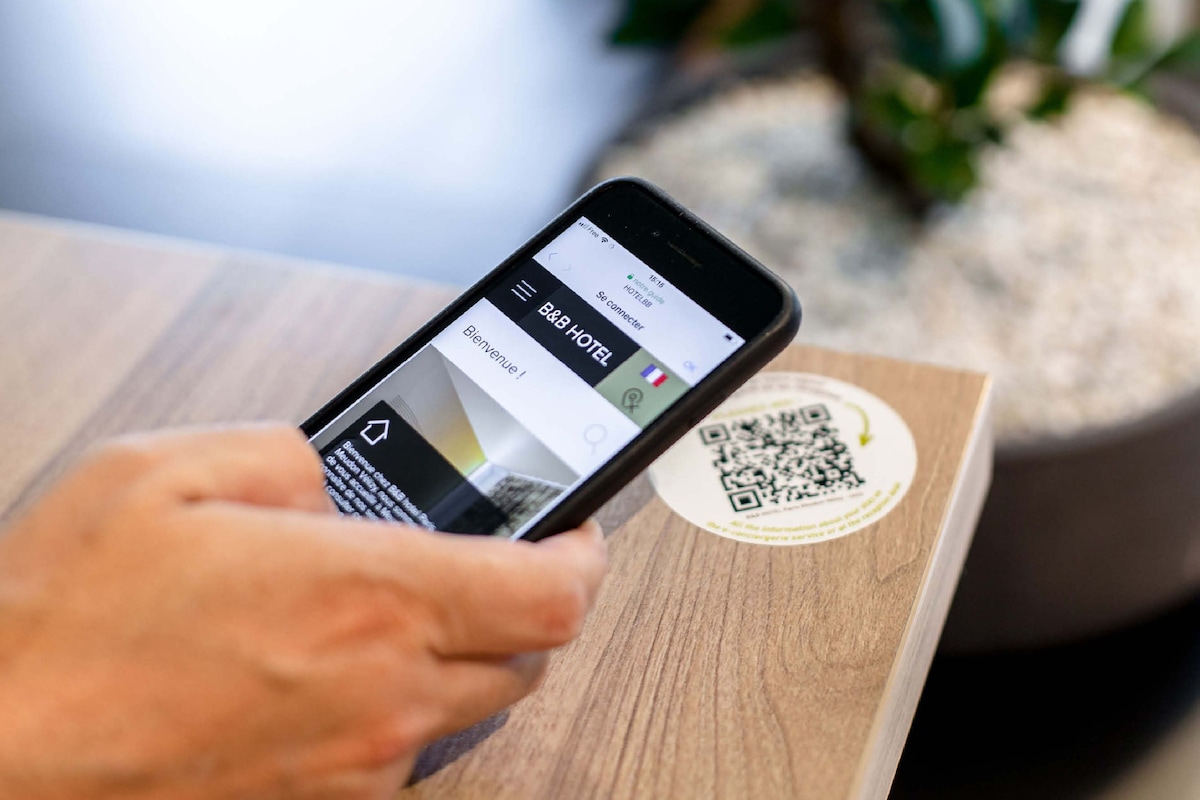 A smartphone displaying a hotel booking app with a QR code on a wooden surface.