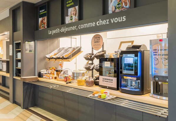 A breakfast counter with a coffee machine, jars of spreads, and a sign welcoming customers.