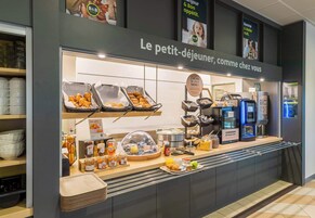 Mostrador de desayuno tipo buffet con diversos alimentos y una máquina de café.