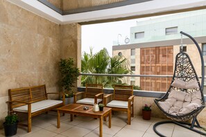 A balcony with a wooden bench, two chairs, a hanging chair, and potted plants.