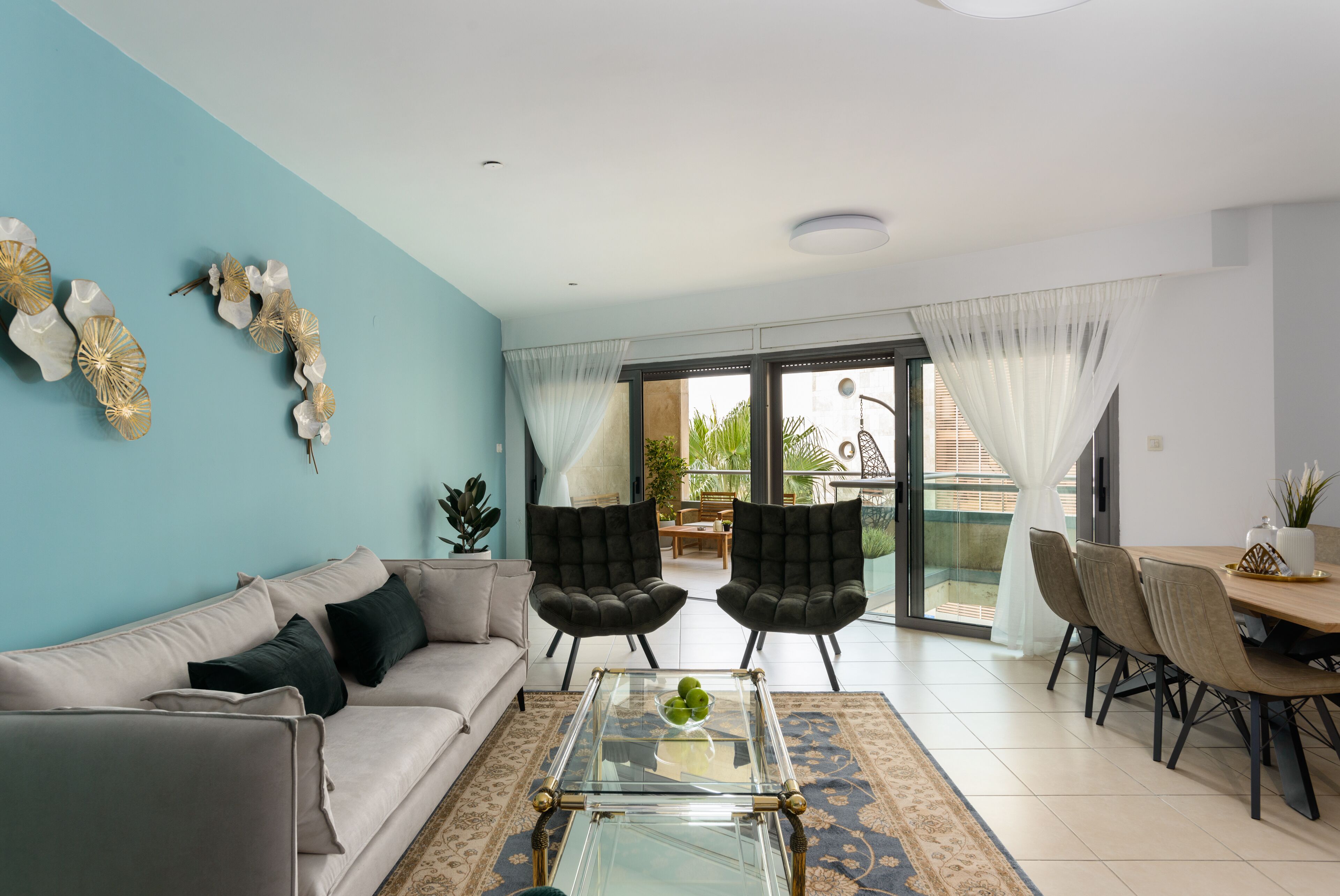 A modern living room with a sofa, two armchairs, a glass coffee table, and a dining area with chairs and a table.