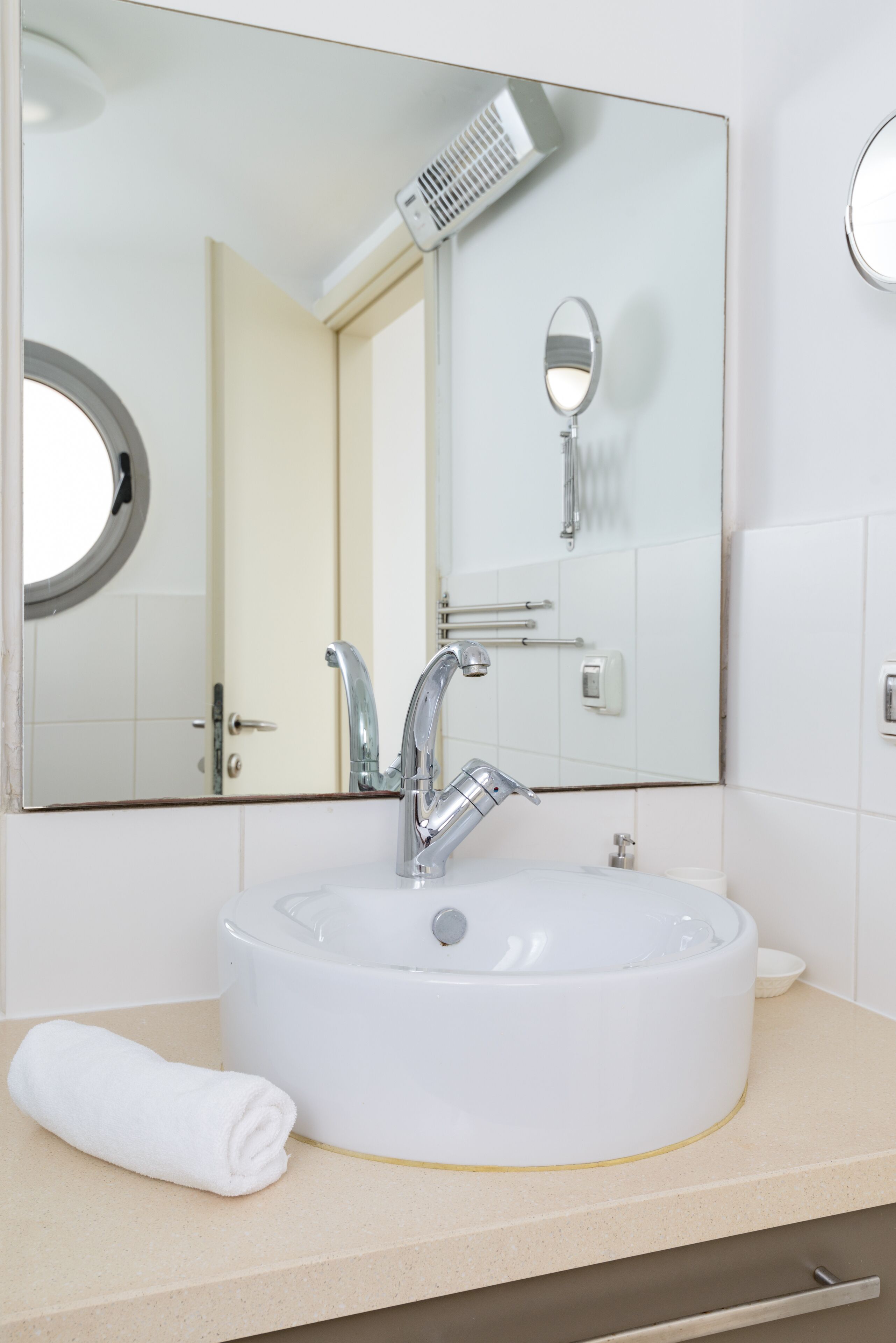Un baño con un espejo redondo, un lavabo blanco, un secador de pelo de mano y una toalla en la encimera.